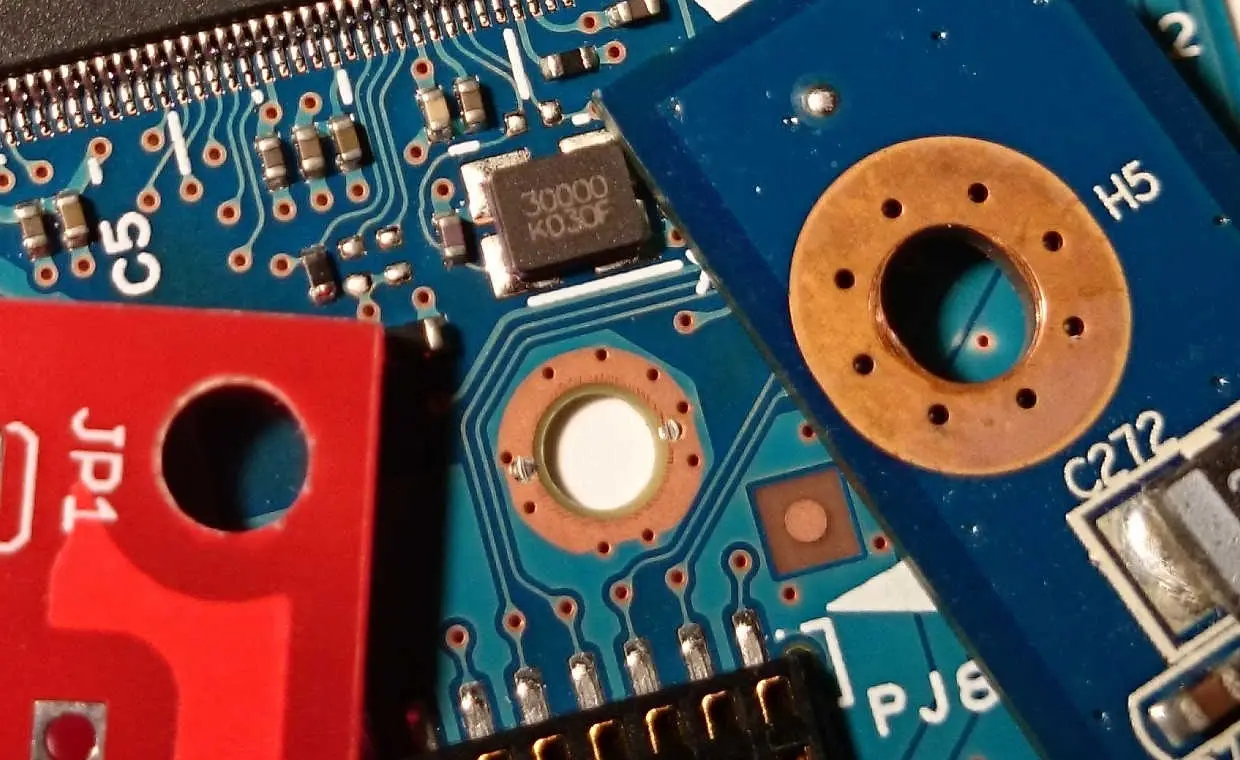 Close-up of a PCB with a visible through-hole via, showing the copper-plated hole used for interlayer electrical connections.