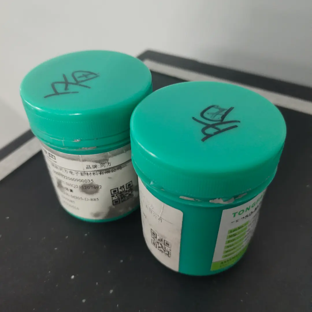 Close-up of solder paste jars with tracking labels for SMT assembly process.