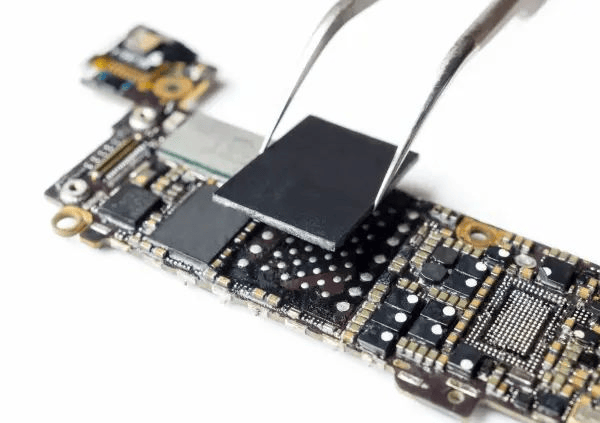 Technician placing a BGA chip onto a high-density automotive PCB using tweezers.