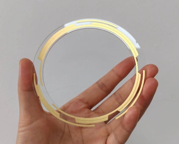 Transparent PCB ring-shaped circuit board held in hand, showing copper traces visible through the clear substrate